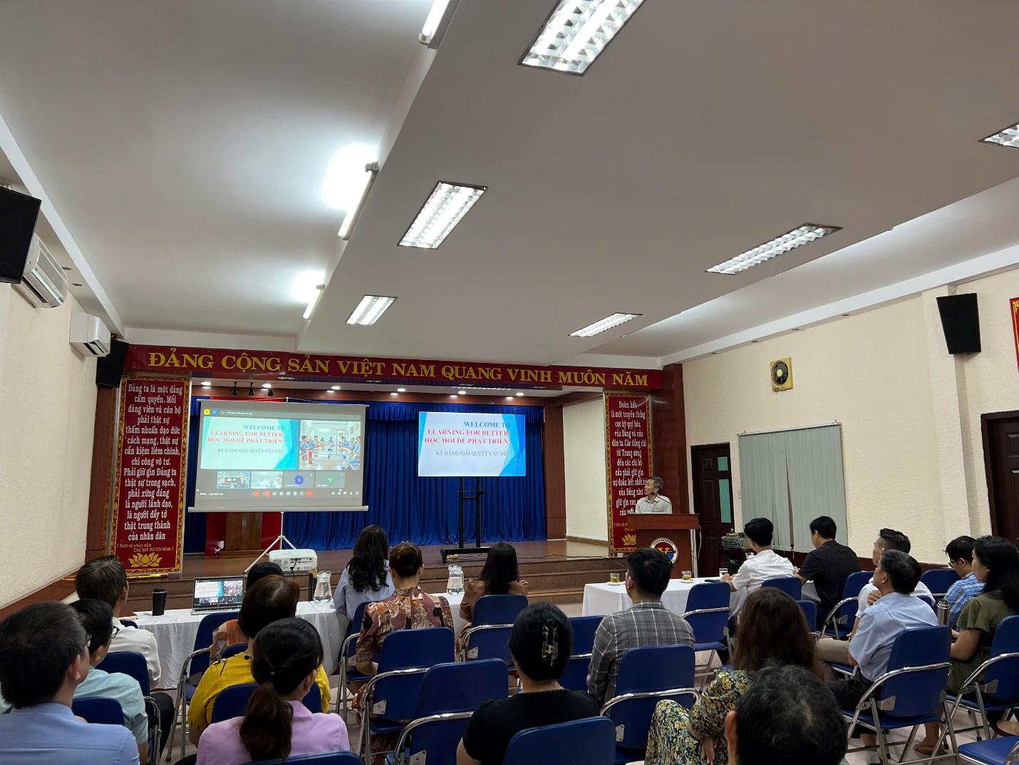 A group of people sitting in chairs in a room with a screen Description automatically generated